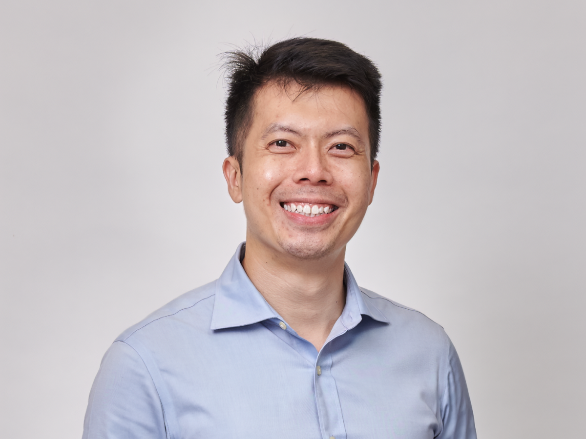 Mr Cham Dao Song in a light blue shirt smiling with one hand in his pocket against a plain background